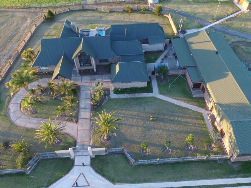 Aerial view of a large farm property featuring a main residence, extensive landscaped gardens, paved pathways, a swimming pool, and outbuildings with solar panels.