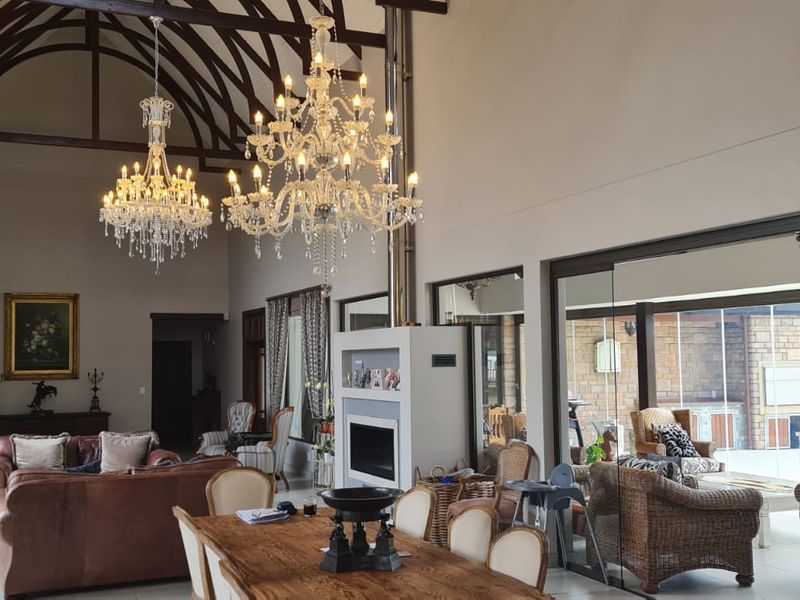 Spacious open-plan living and dining area featuring high vaulted ceilings with exposed timber trusses, a central fireplace, and large glass doors leading to the patio.