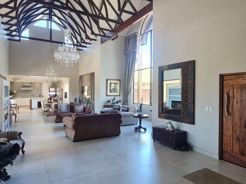 Spacious open-plan living area featuring a dramatic vaulted ceiling with exposed timber trusses, large arched windows, tiled flooring, and a grand entrance.