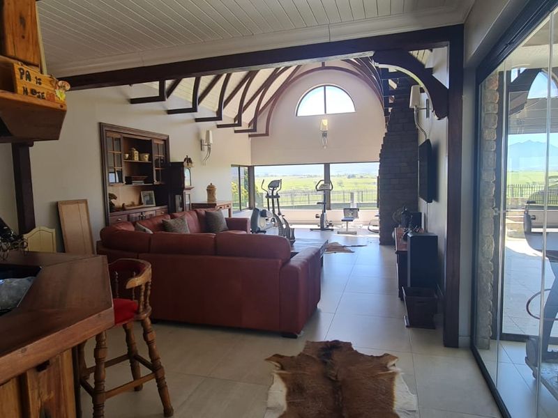 Spacious open-plan living area featuring exposed timber trusses, a stone fireplace, and large glass sliding doors opening to a scenic outdoor patio.