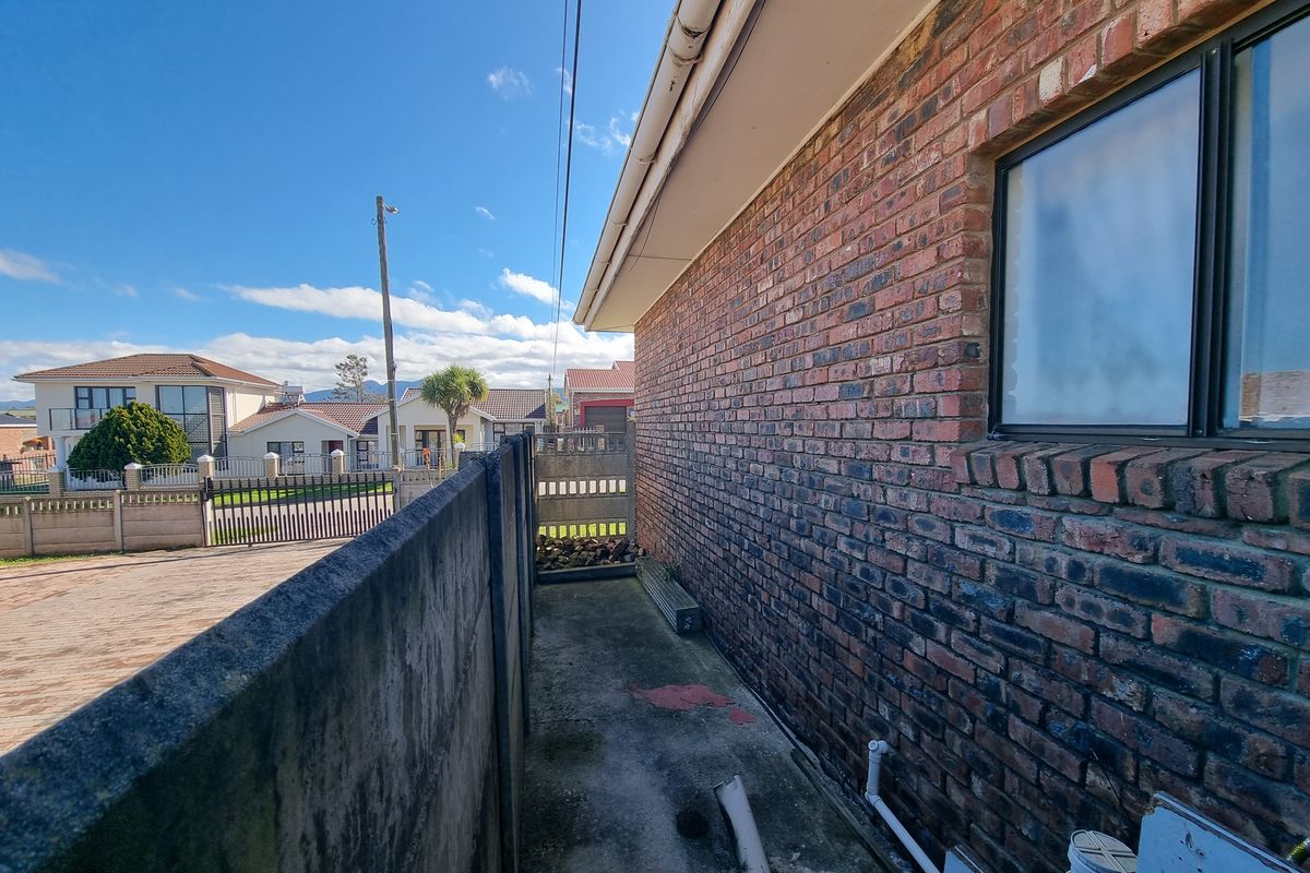 A narrow side passage featuring a brick exterior wall, concrete paving, and a precast boundary wall in a residential setting.