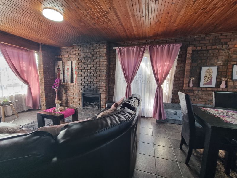 Open plan living and dining area featuring exposed brick walls, a built-in fireplace, and a timber ceiling with tiled flooring throughout.