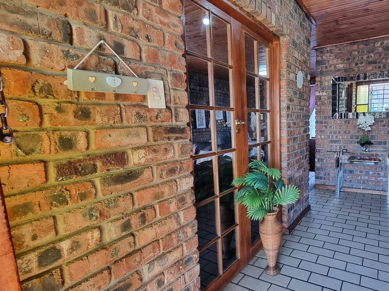 A covered patio area featuring exposed brick walls, a timber paneled ceiling, and timber-framed glass double doors leading into the home.