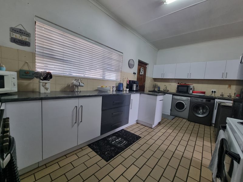 A functional kitchen featuring white and dark grey cabinetry, laminate countertops, tiled flooring, and integrated laundry facilities with a tiled backsplash.