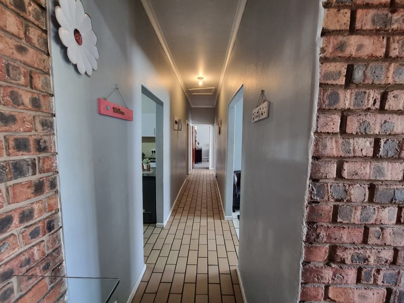 A long interior hallway featuring exposed brick accents and tiled flooring, providing access to multiple rooms within the home.