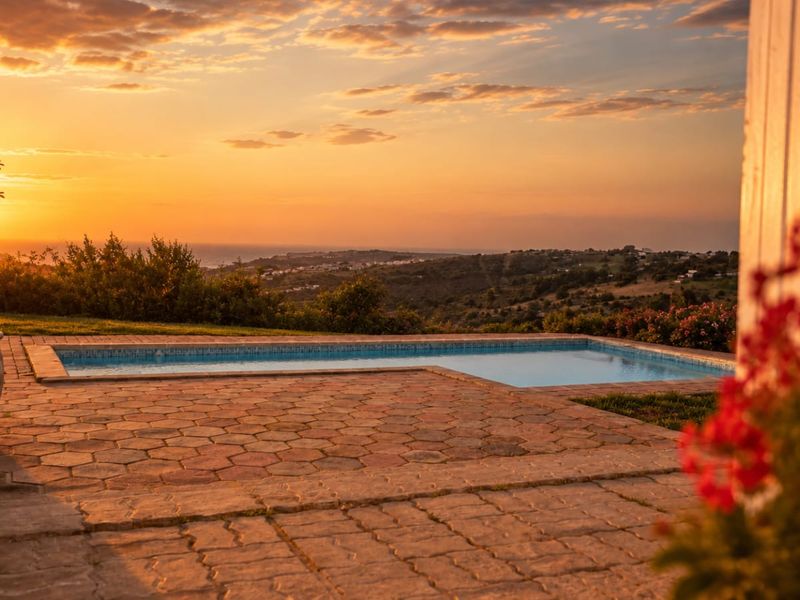 A scenic outdoor pool area featuring a paved patio and expansive sunset views over the surrounding landscape.