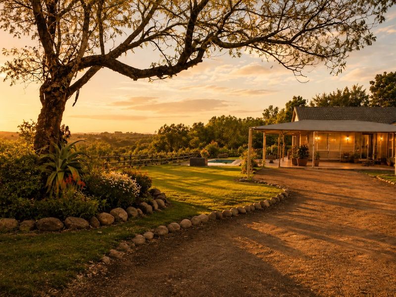 A scenic rear view of a small holding featuring a covered patio, swimming pool, and expansive garden at sunset.
