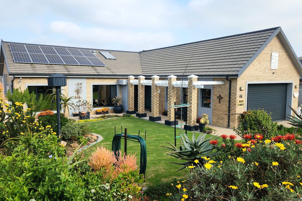 A well-maintained brick house featuring a landscaped garden, a pergola-covered patio area, and roof-mounted solar panels.