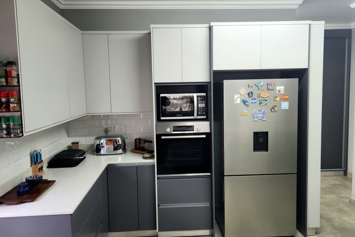 Modern kitchen featuring two-tone cabinetry, quartz countertops, subway tile backsplash, and integrated stainless steel appliances including an oven and microwave.