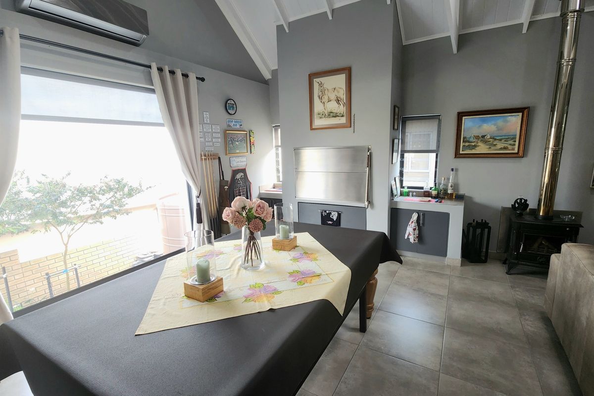 Spacious living area featuring a vaulted ceiling with exposed rafters, a built-in braai, a wood-burning stove, and tiled flooring.