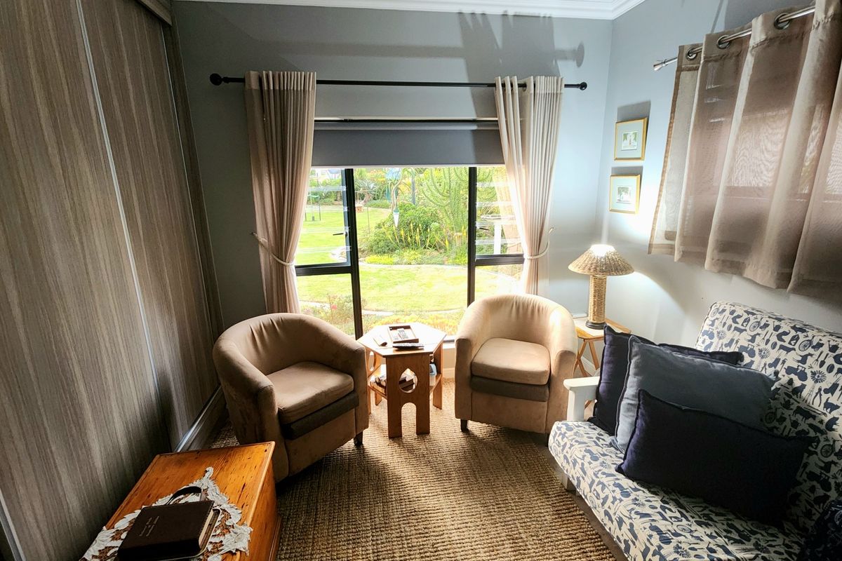 A cozy living area featuring built-in sliding door wardrobes, carpeted flooring, and a large window overlooking the garden.