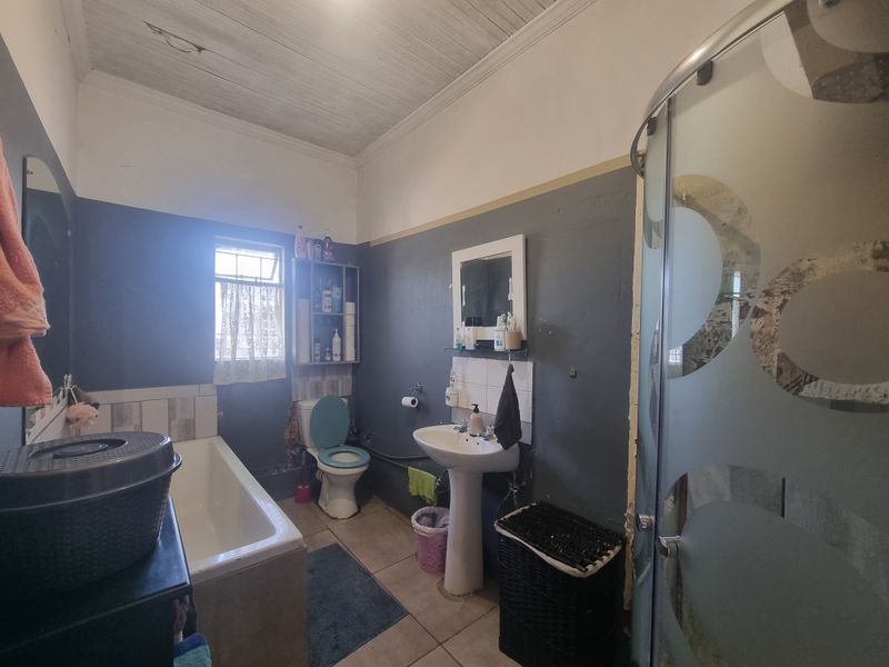 A dated bathroom featuring a pedestal basin, bathtub, and separate shower enclosure with timber ceiling and tiled flooring.