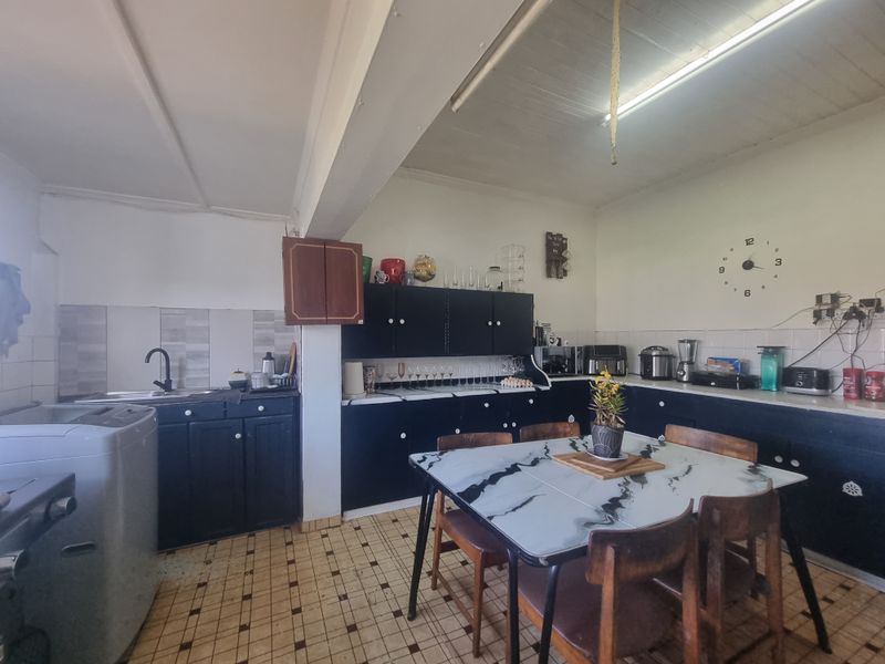 Open-plan kitchen and dining area featuring dark cabinetry, tiled backsplash, and original tiled flooring, offering potential for a modern renovation.