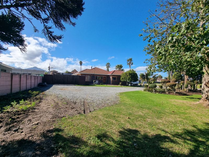 Front view of the residential property featuring a gravel driveway, established garden, and boundary wall, showcasing the exterior facade and grounds.