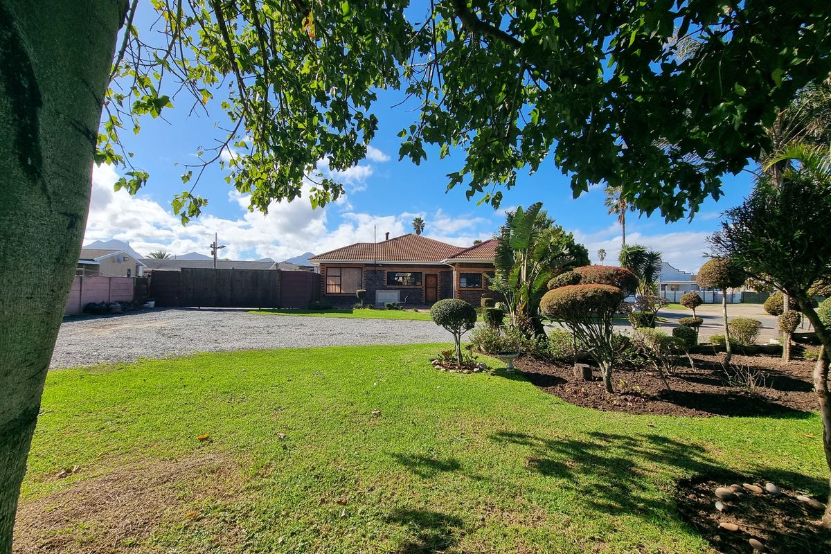 Front view of a residential property featuring a well-maintained garden, gravel driveway, and brick exterior with a tiled roof.