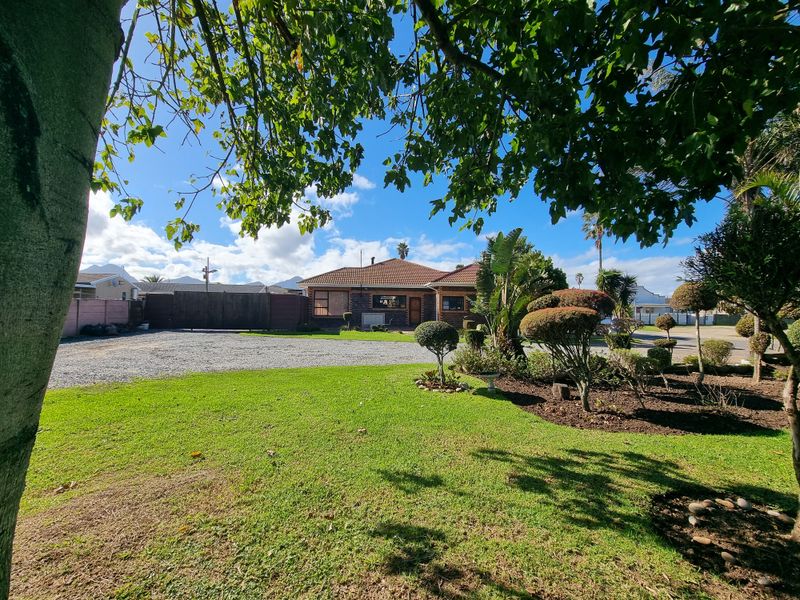 Front view of a residential property featuring a well-maintained garden, gravel driveway, and brick exterior with a tiled roof.