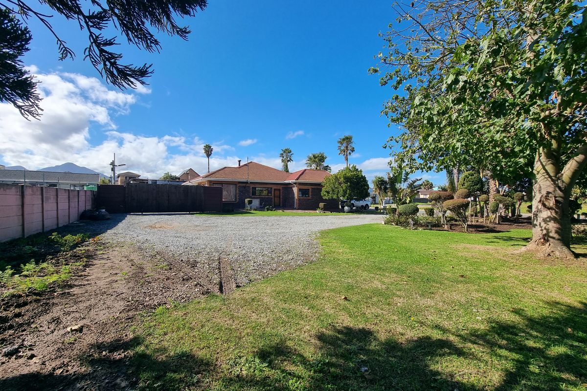 Front view of the residential property featuring a gravel driveway, established garden, and boundary wall.