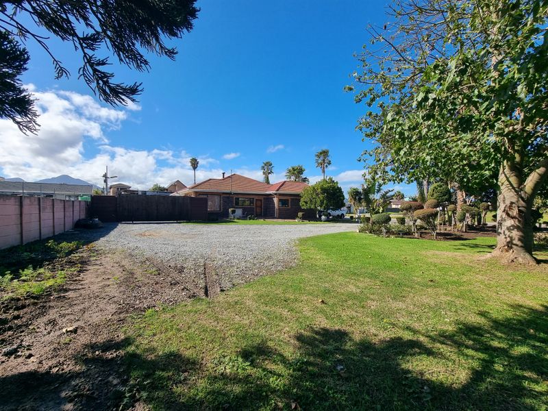 Front view of the residential property featuring a gravel driveway, established garden, and boundary wall.