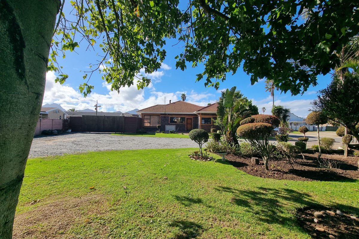 Front view of a residential property featuring a well-maintained garden, gravel driveway, and traditional brick facade with a tiled roof.