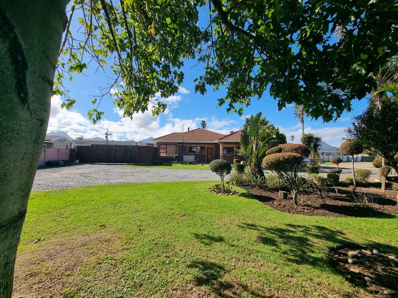 Front view of a residential property featuring a well-maintained garden, gravel driveway, and traditional brick facade with a tiled roof.