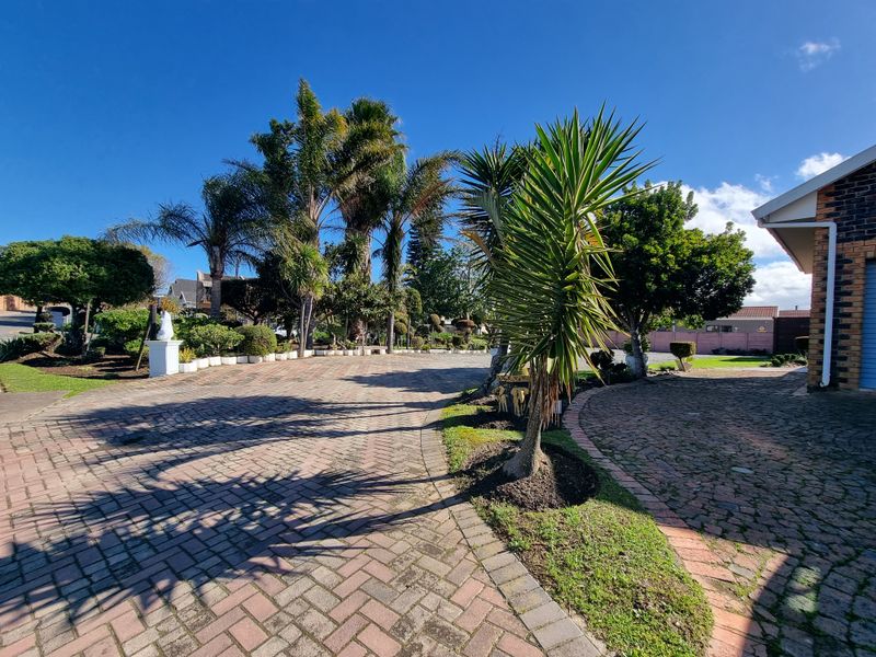 A well-maintained front exterior view featuring a spacious paved driveway and established garden landscaping leading toward the residential property.