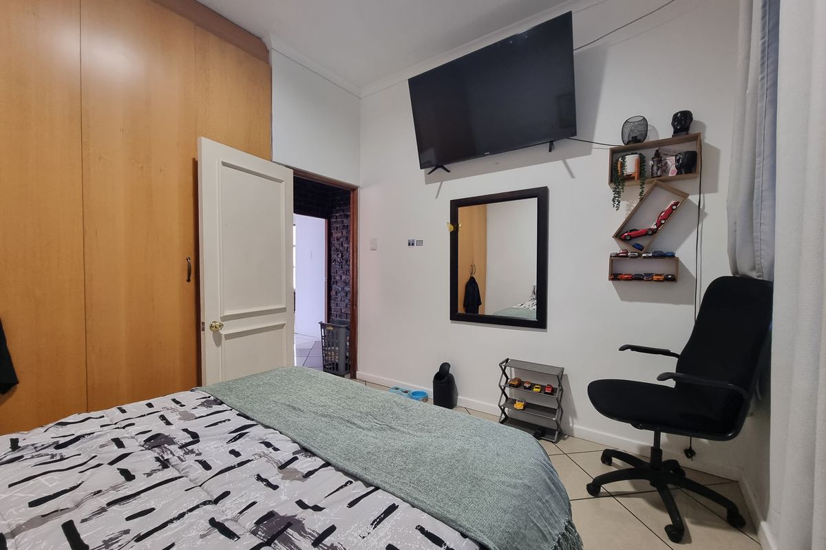 A bedroom featuring built-in wooden cupboards, tiled flooring, and a neutral wall finish, providing a functional living space.