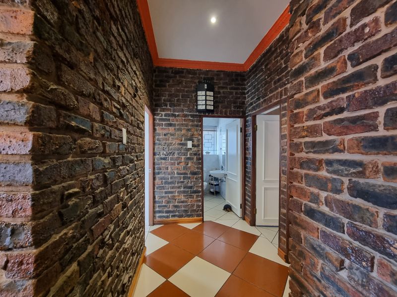 A hallway featuring exposed brick walls, patterned ceramic tile flooring, and decorative orange-painted cornicing, providing access to adjacent rooms.
