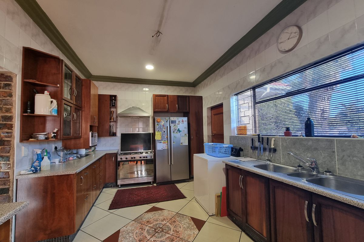 A functional kitchen featuring wooden cabinetry, laminate countertops, a gas stove with extractor, and tiled flooring with a decorative inlay.