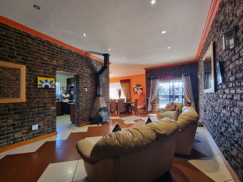 Spacious open-plan living and dining area featuring exposed brick walls, a central freestanding fireplace, and tiled flooring with recessed lighting.