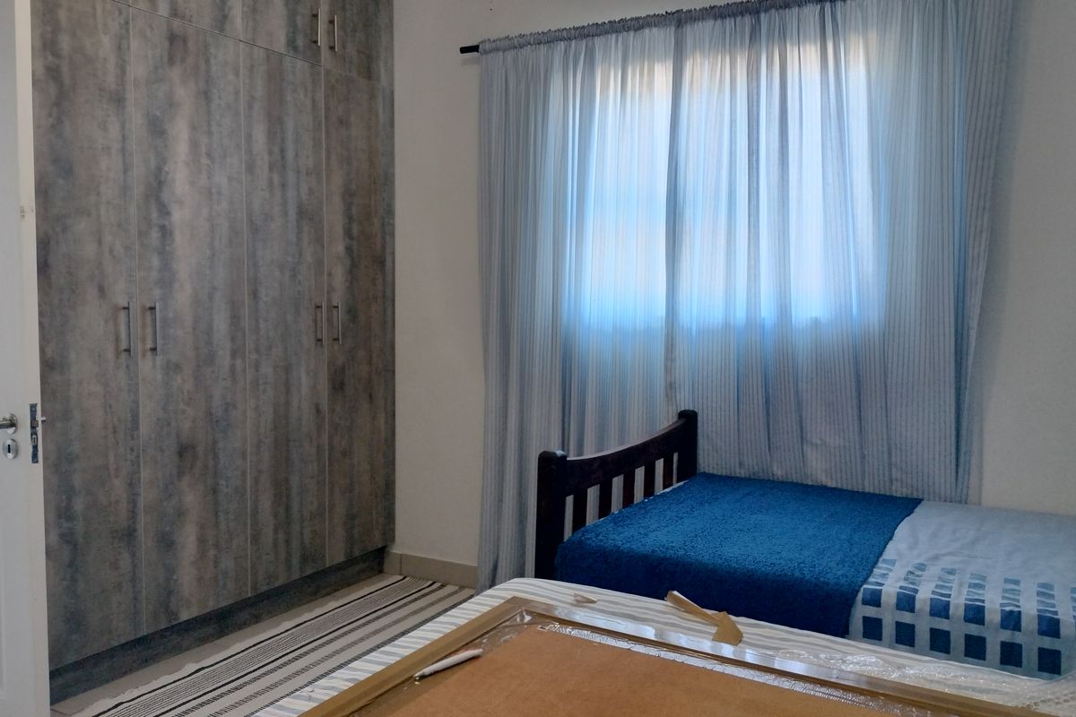 A bedroom featuring floor-to-ceiling built-in cupboards with a wood-grain finish and natural light filtering through window curtains.