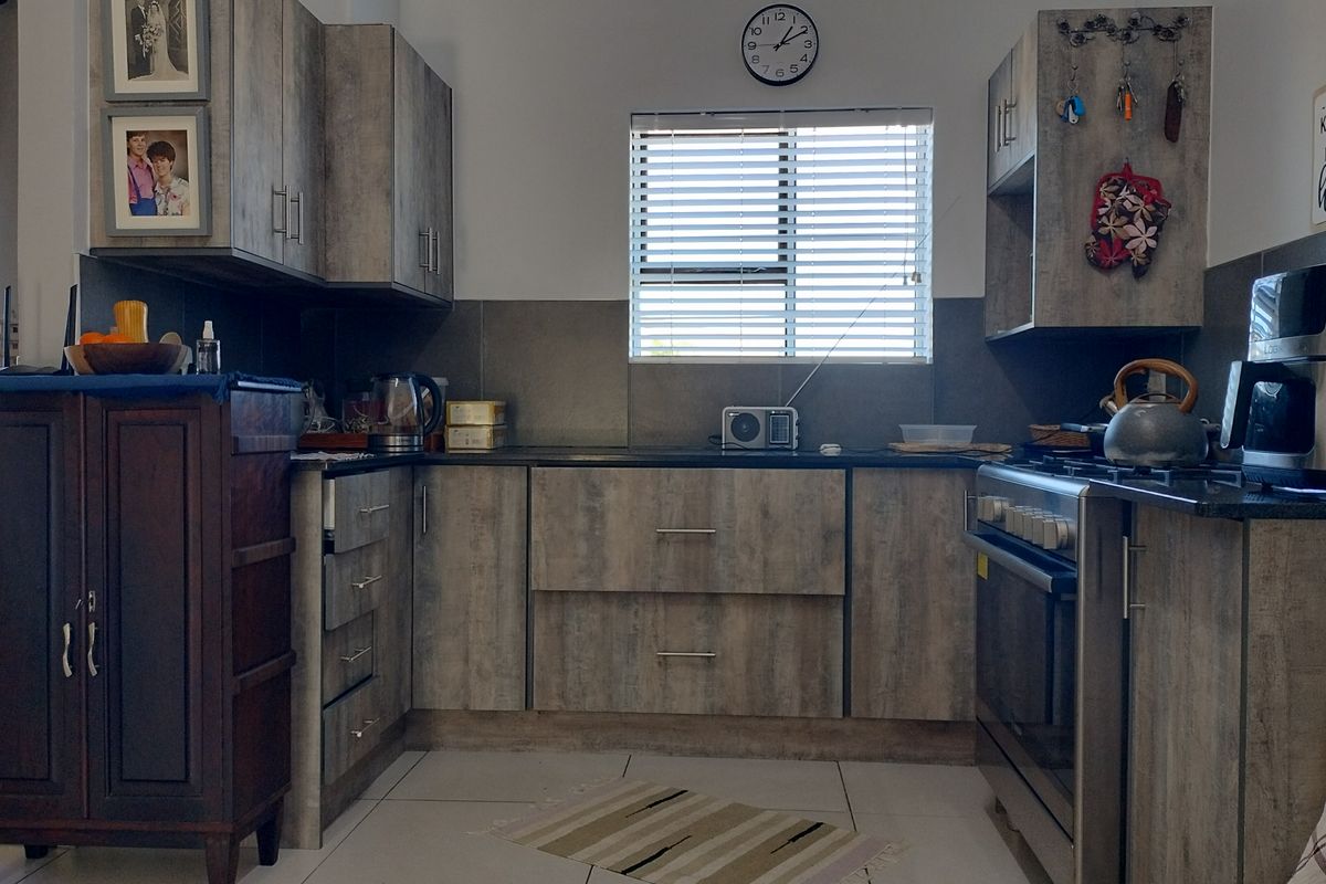 A functional kitchen featuring modern wood-look laminate cabinetry, stone countertops, a tiled splashback, and a freestanding oven with hob.