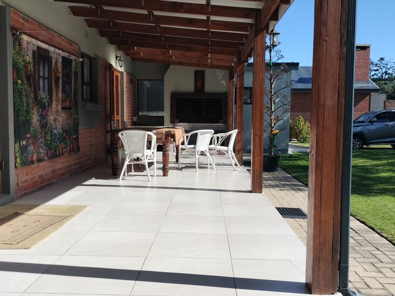 Covered outdoor patio featuring a timber pergola, tiled flooring, and a built-in braai, overlooking the rear garden area.
