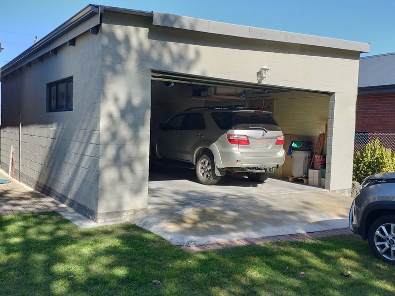 A detached single-car garage featuring concrete block construction and a concrete driveway, situated in a residential garden setting.
