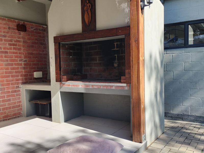 Outdoor patio area featuring a built-in brick braai, tiled flooring, and a combination of face brick and rendered masonry walls.