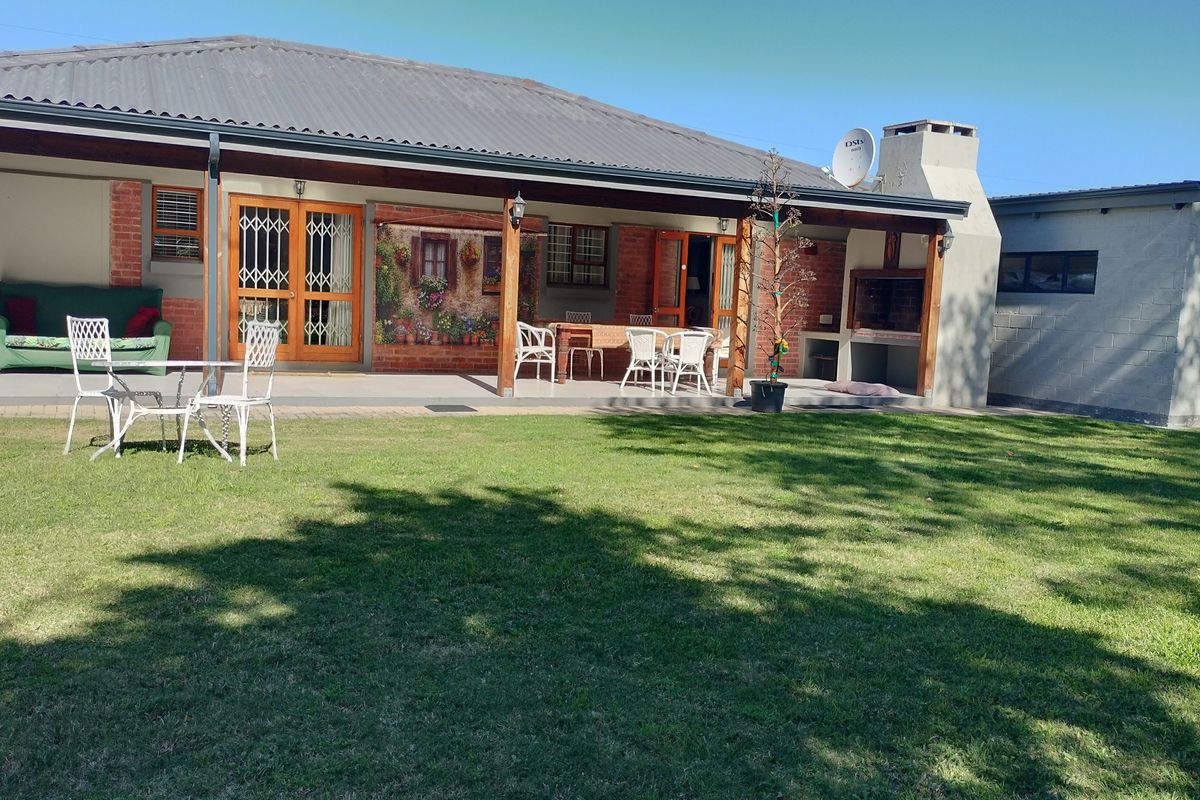 Spacious covered rear patio featuring a built-in braai, brick accents, and direct access to the garden area.