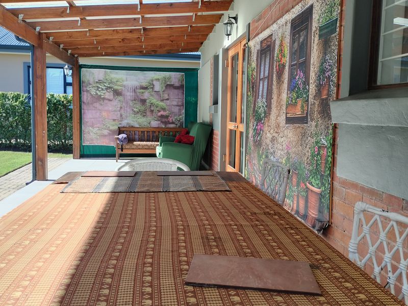 A covered outdoor patio area featuring a timber pergola structure, brick wall detailing, and paved flooring, suitable for alfresco dining and relaxation.