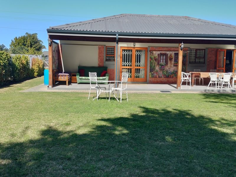 A spacious covered rear patio featuring brick detailing and security gates, overlooking a well-maintained garden lawn.