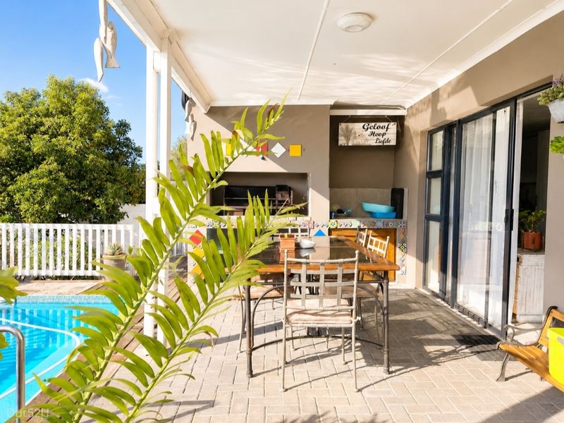 A covered outdoor patio featuring a built-in braai, paved flooring, and direct access to the swimming pool area.