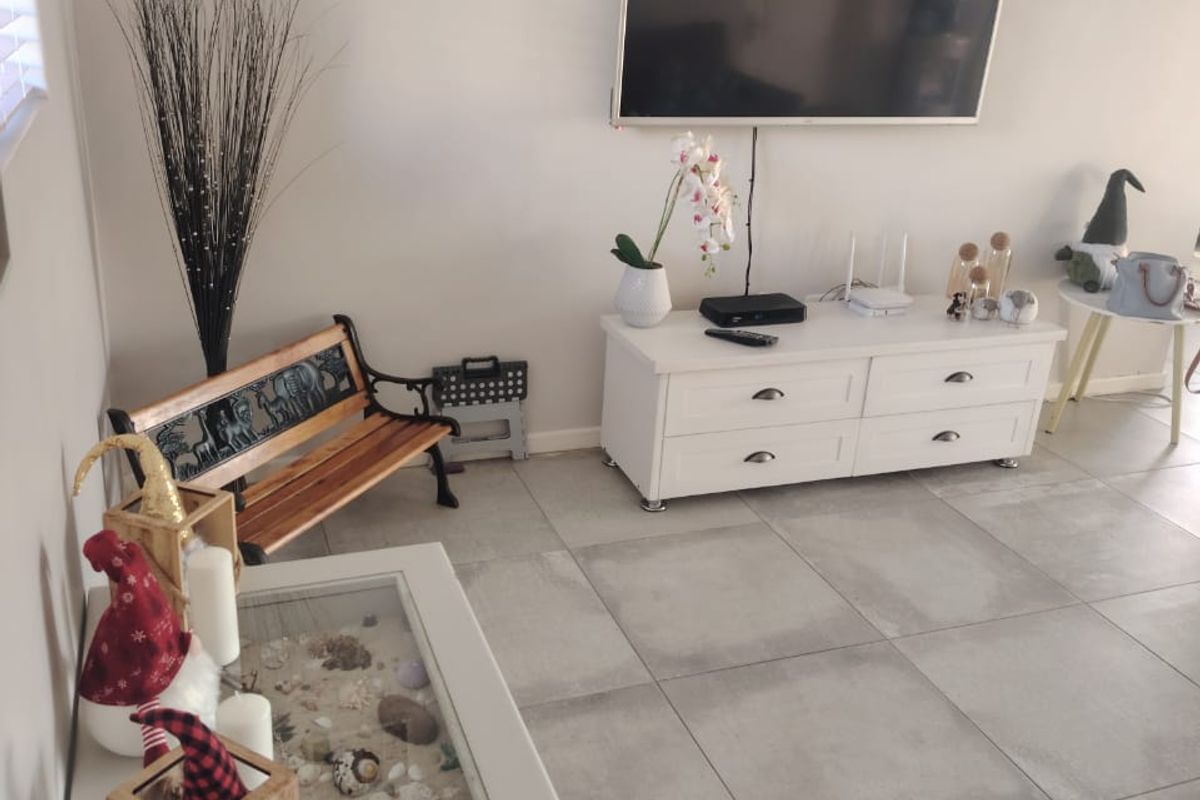 A bright living room featuring large format floor tiles and a wall-mounted television, offering a clean and neutral foundation for living space.