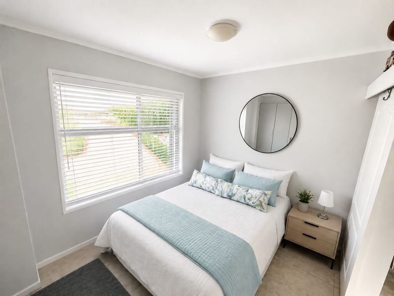 A bright and well-maintained bedroom featuring neutral wall tones, tiled flooring, a built-in wardrobe, and large window with venetian blinds.