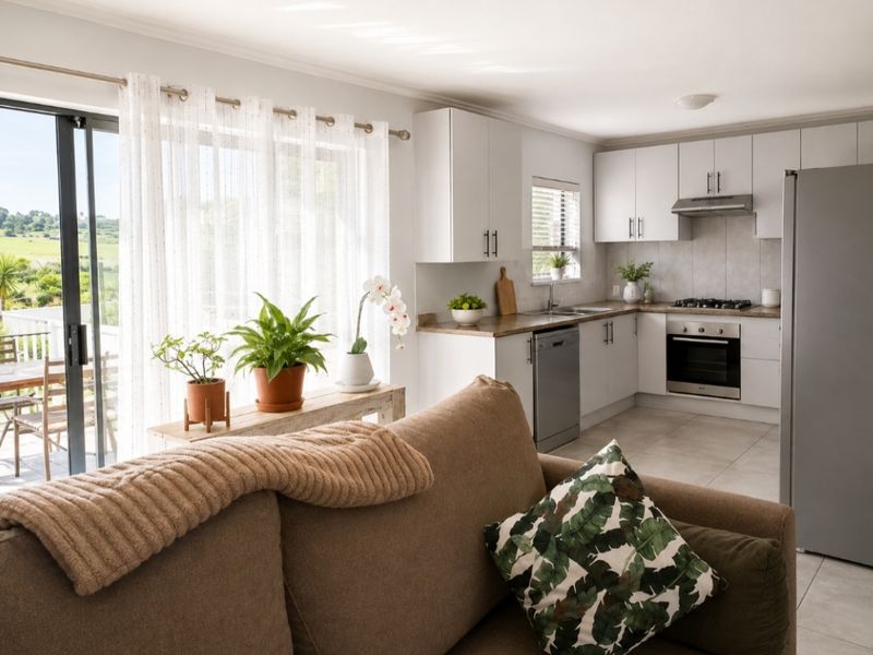 Bright open-plan kitchen and living area featuring modern white cabinetry, integrated appliances, tiled flooring, and direct access to an outdoor patio through sliding doors.