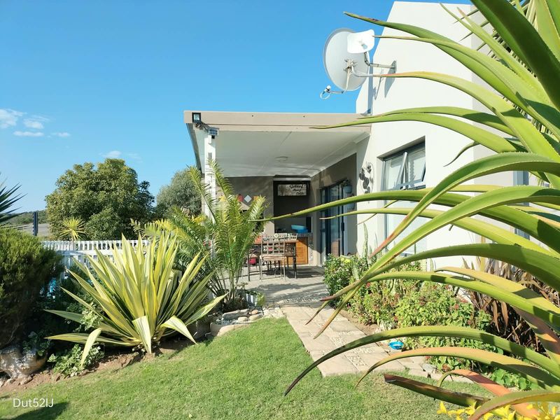 A covered outdoor patio area featuring paved flooring and exterior lighting, adjacent to a landscaped garden and lawn.