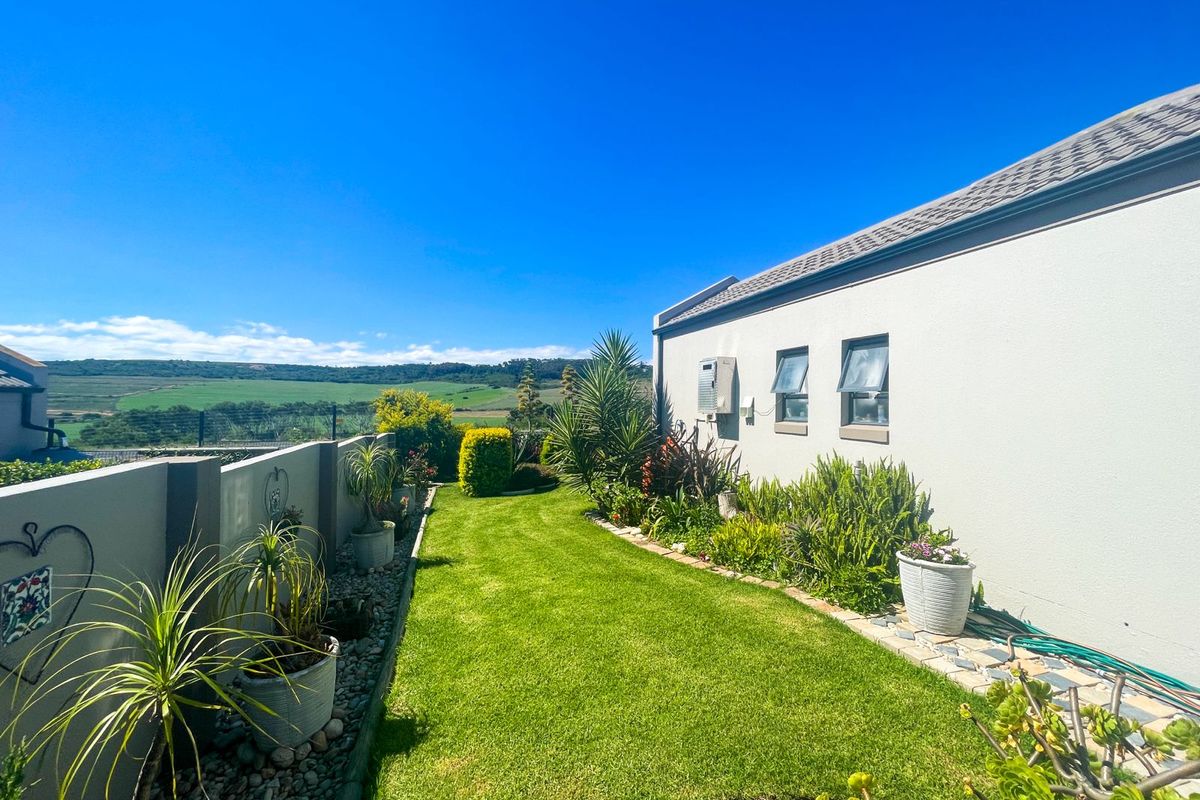 A well-maintained rear garden featuring a manicured lawn, boundary wall, and scenic landscape views, adjacent to the side elevation of the house.