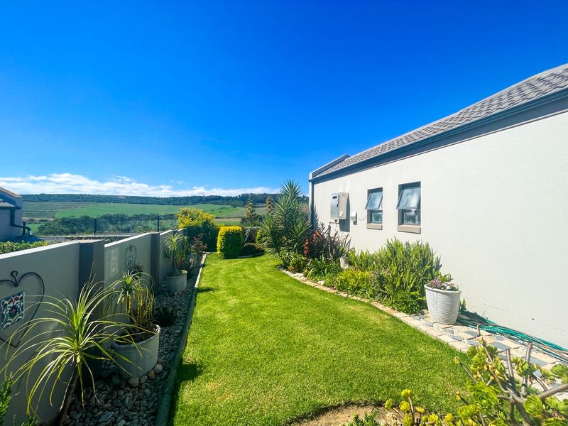 A well-maintained rear garden featuring a manicured lawn, boundary wall, and scenic landscape views, adjacent to the side elevation of the house.