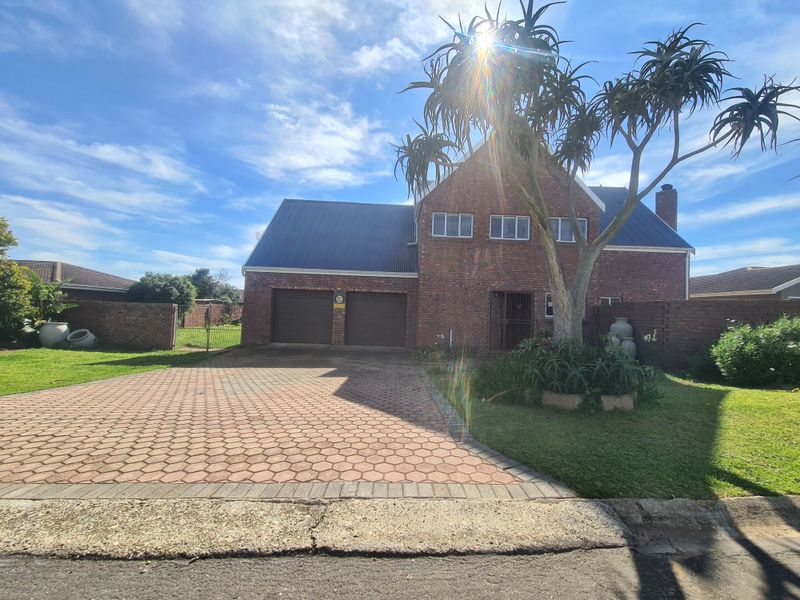 Front view of a double-story brick house featuring a paved driveway, double garage, and established garden.