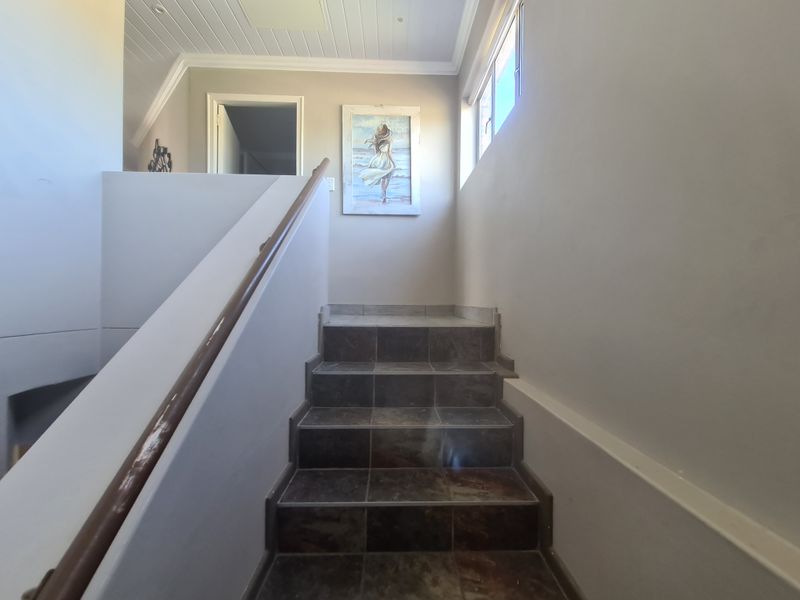 A staircase featuring dark tiled steps, a timber handrail, and a white tongue and groove ceiling, leading to an upper landing area.