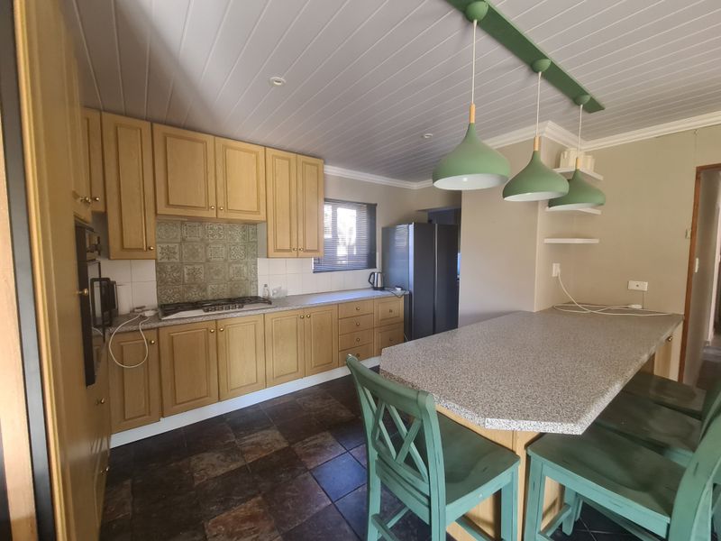 A functional kitchen featuring light wood cabinetry, a gas hob, tiled splashback, and a breakfast bar with stone-look countertops.