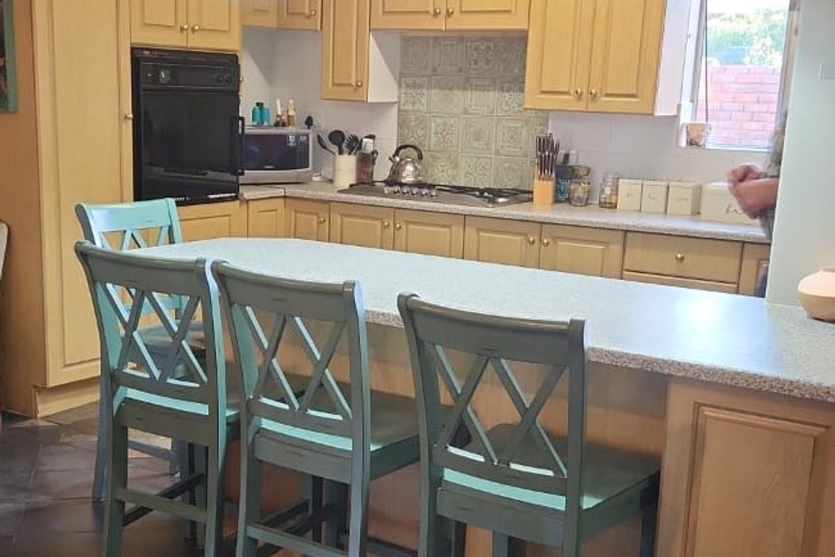 A functional kitchen featuring wooden cabinetry, a central island with seating, built-in oven, hob, and decorative pendant lighting.