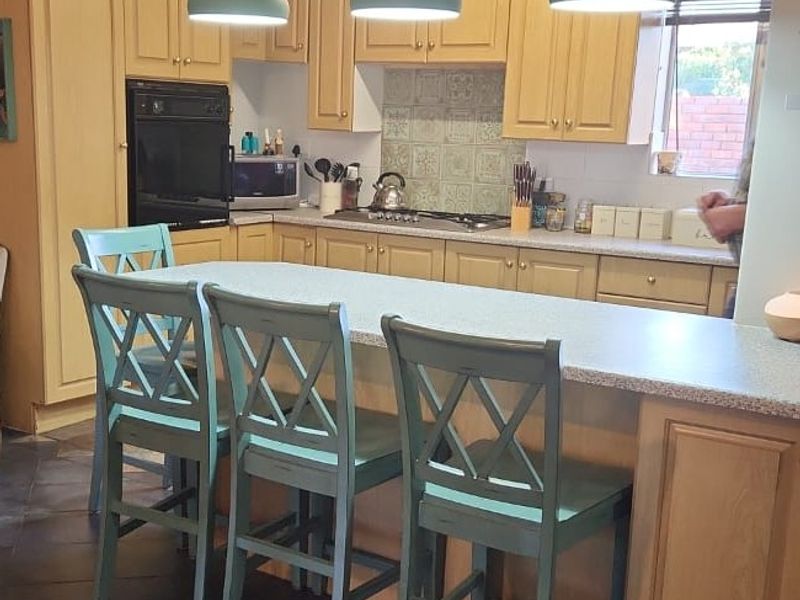 A functional kitchen featuring wooden cabinetry, a central island with seating, built-in oven, hob, and decorative pendant lighting.