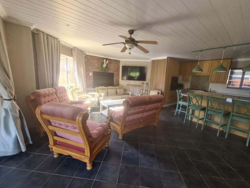 Spacious open-plan living and kitchen area featuring a brick fireplace, timber cabinetry, kitchen island, and tiled flooring throughout.